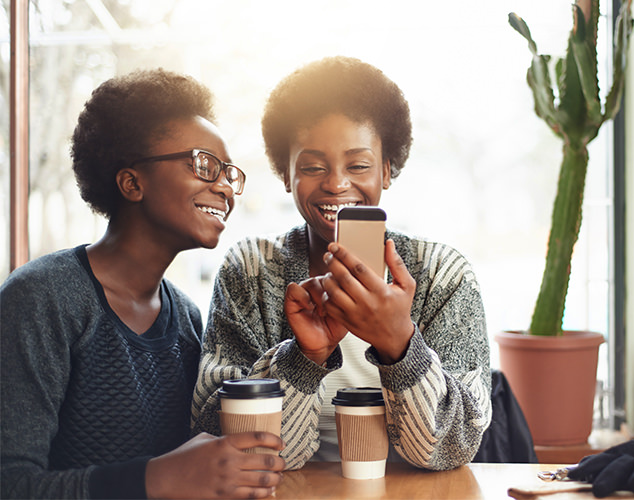 Two women drinking coffee and looking at smartphone